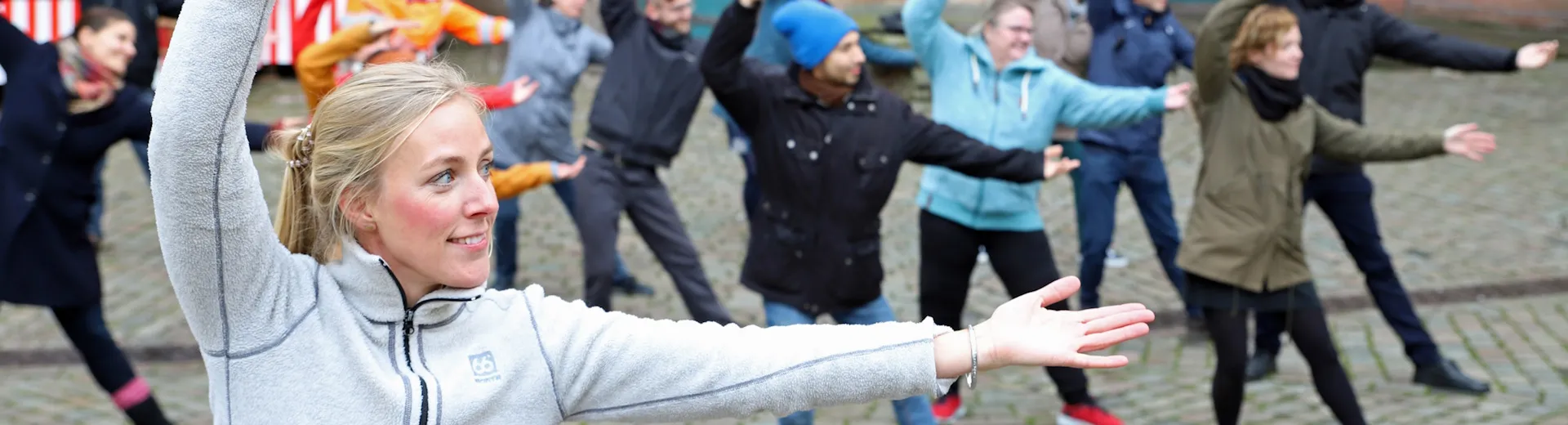Offenes Bewegungsangebot der Stadt Marburg: Eine Gruppe von Menschen macht Qi-Gong-Übungen auf dem Marktplatz. Verteilseite Sport und Gesundheit
