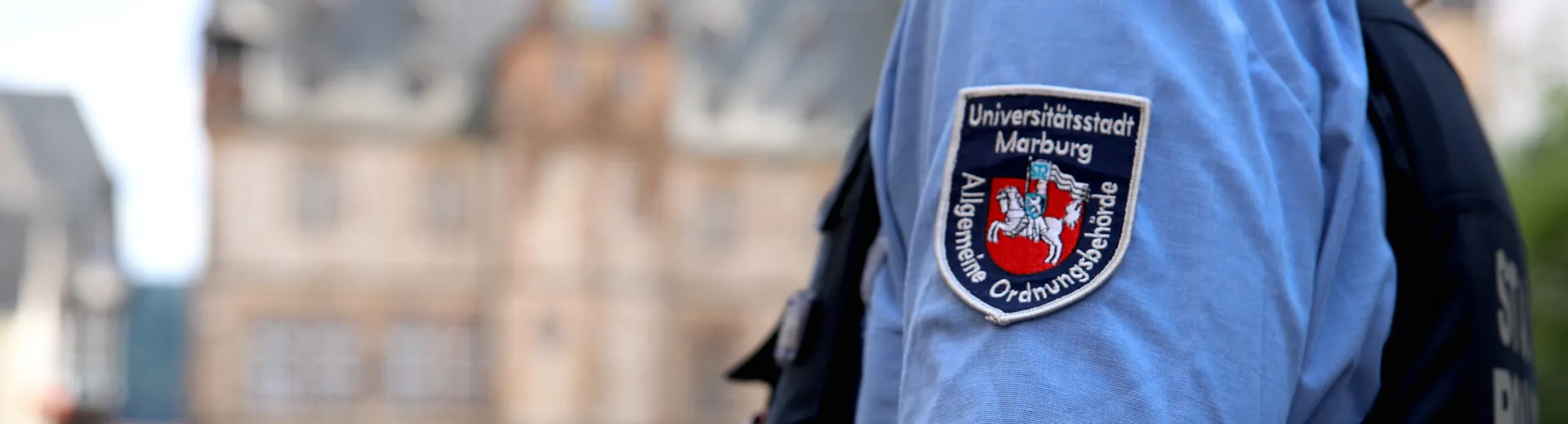 Ein Mitarbeiter der Stadtpolizei in Uniform. Im Hintergrund das Marburger Rathaus. Verteilseite Sicherheit und Ordnung - Stadtpolizei Uniform
