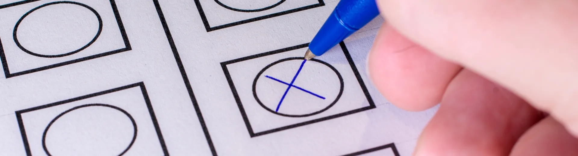 Detailaufnahme von einer Hand, die einen Kuli hält und ein Kreuz auf einem Wahlschein macht. Verteilseite Wahlen und Wahlergebnisse, Kreuz und Hand