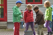 4 Kinder in Regenkleidung stehen um einen Eimer herum und scheinen etwas anzurühren.