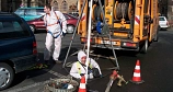 Das Bild zeigt einen Mitarbeiter des DBM, der bereits bis zur Körpermitte in einen Schacht hinabgestiegen ist. Er ist durch ein Seil gesichert und trägt einen Ganzkörperanzug.