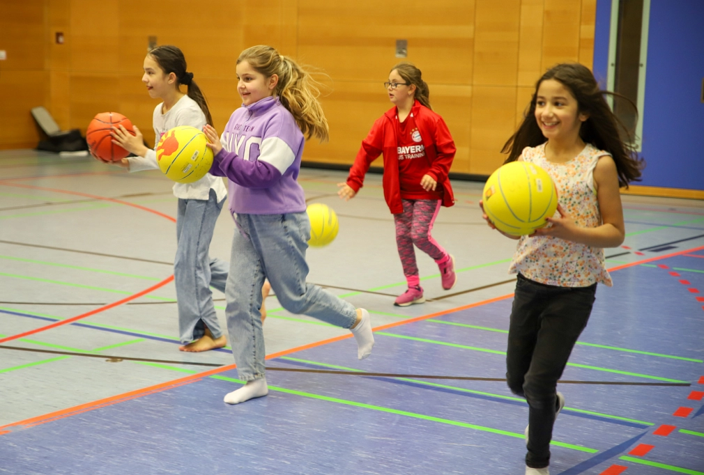Angebot über SPORT VERNETZT: Basketball-Mädchen-AG an der Astrid-Lindgren-Schule. Lachende Mädchen laufen mit Basketbällen durch eine Sporthalle. © Simone Batz, Stadt Marburg