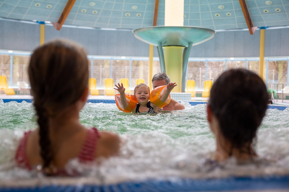 Im Whirlpool des AquaMar ist eine Familie zu sehen: Das kleine Mädchen mit Schwimmflügeln ist im Fokus. Sie planscht fröhlich und lacht. Im Hintergrund hält sie ein Mann mit grauen Haaren. Im Vordergrund sind verschwommen zu sehen ein Mädchen und eine Frau, die den Rücken der Kamera zugewandt haben und zu dem kleinen Mädchen blicken.&nbsp;&copy;&nbsp;Patricia Grähling, Stadt Marburg