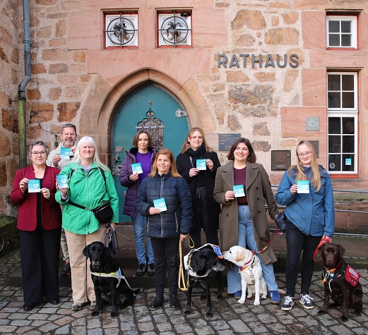 Vor der Eingangstür des Marburger Rathauses stehen Menschen und Hunde. Die Menschen halten einen Aufkleber in der Hand.