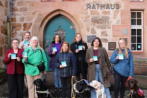Assistenzhund willkommen Vor der Eingangstür des Marburger Rathauses stehen Menschen und Hunde. Die Menschen halten einen Aufkleber in der Hand.