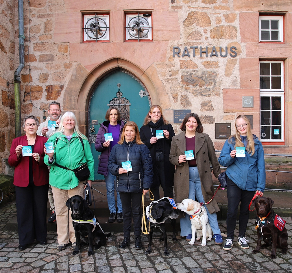 Vor der Eingangstür des Marburger Rathauses stehen Menschen und Hunde. Die Menschen halten einen Aufkleber in der Hand.