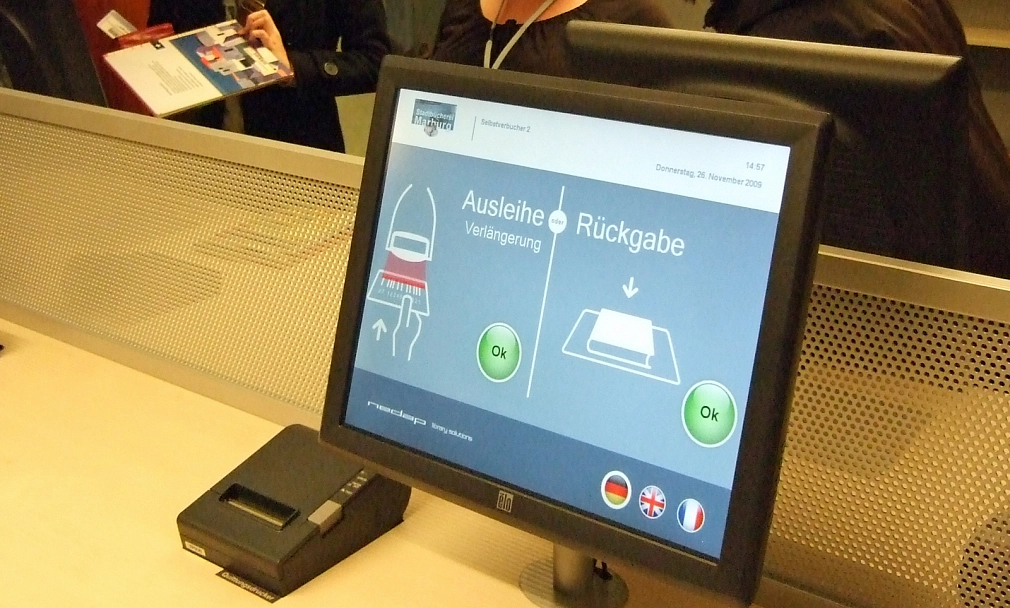 Ein Bildschirm in der Stadtbücherei: Der Screen zeigt die beiden Optionen "Ausleihe - Verlängerung" und "Rückgabe". Neben den beiden Optionen ist jeweils ein grünes, rundes "Ok"-Feld zu sehen, das per Fingerdruck angewählt werden kann.&nbsp;&copy;&nbsp;Universitätsstadt Marburg