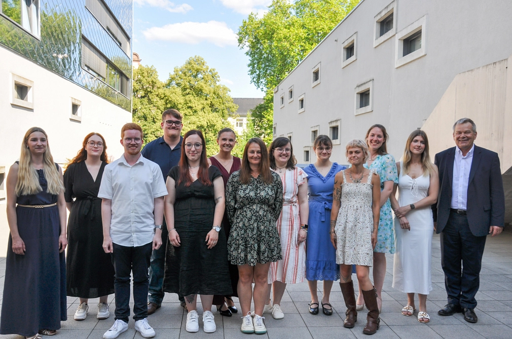 Auf dem Bild sieht man 14 Personen, gemischt aus Damen und Herren, die alle glücklich und zufrieden in die Kamera schauen.