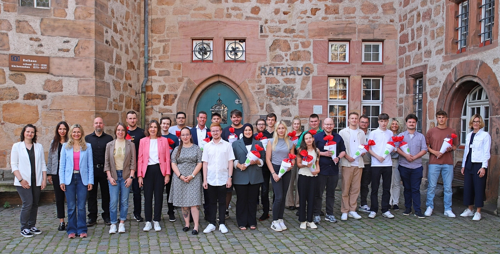 Das Bild zeigt ein Gruppenbild mit den neuen Azubis und deren Willkommenspräsenten vor dem Marburger Rathaus.
