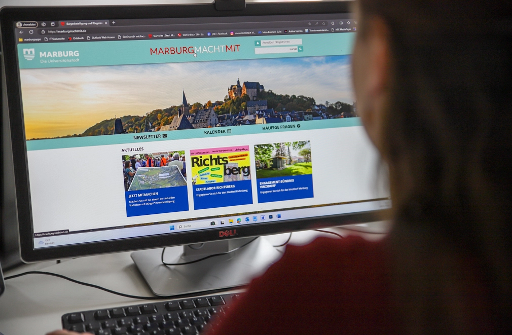Eine Person sitzt vor einem Computer-Bildschirm. Darauf ist die Startseite der Beteiligungsplattform www.marburgmachtmit.de zu sehen.
