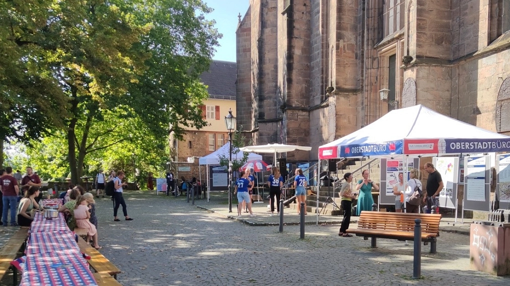 Beteiligungsverfahren Lebendige Oberstadt Lutherischer Kirchhof (Stadtbalkon) mit Informationsständen, Tischen, Bänken und interessierten Menschen. © UmbauStadt PartGmbB