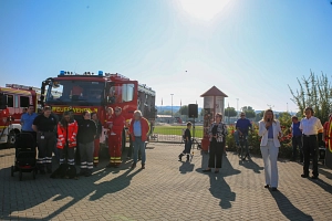 Blaulichttag 2024 Das Bild zeigt links ein Feuerwehrauto, vor dem Menschen stehen, und rechts zwei Frauen, die ein Mikrofon in der Hand halten und hinein sprechen.