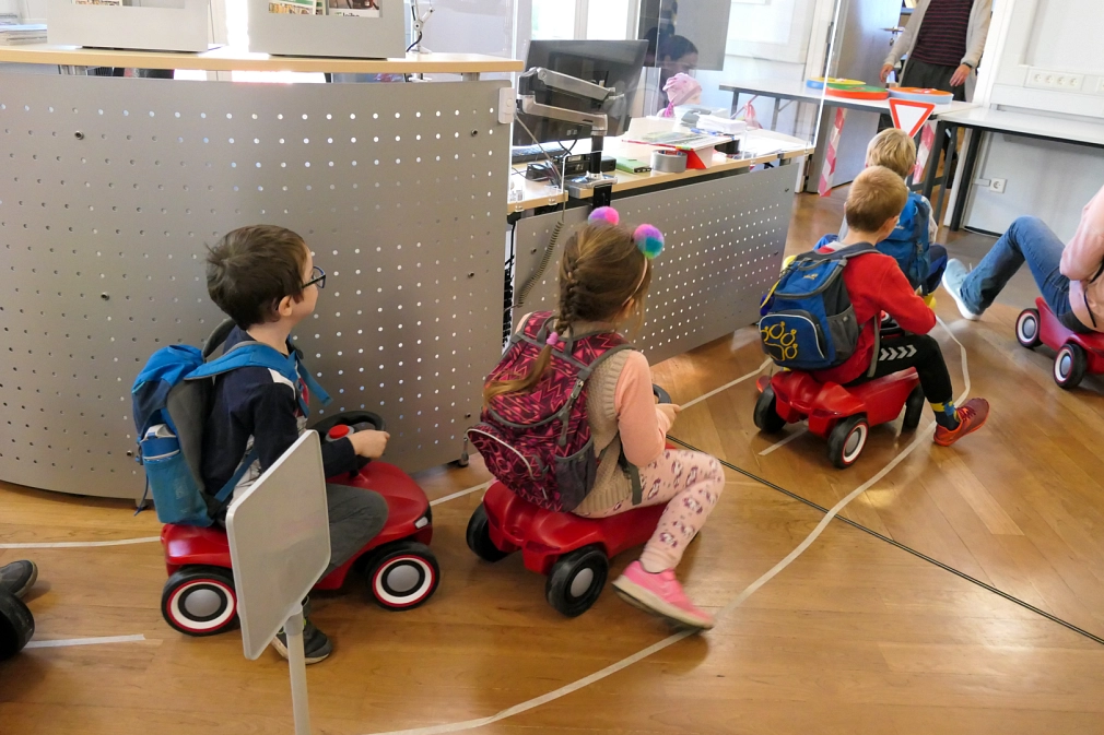 Kinder auf Bobbycars fahren durch die Stadtbücherei