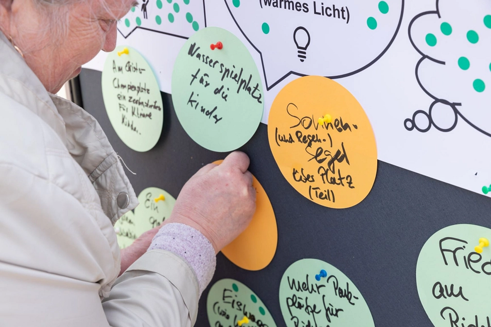 Bürger*innenbeteiligung: Eine ältere Frau heftet eine Karte an eine Pinnwand.