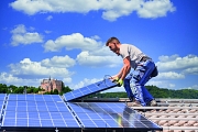 Zwei Männer installieren eine Photovoltaikanlage auf einem Dach. Im Hintergrund das Marburger Schloss.