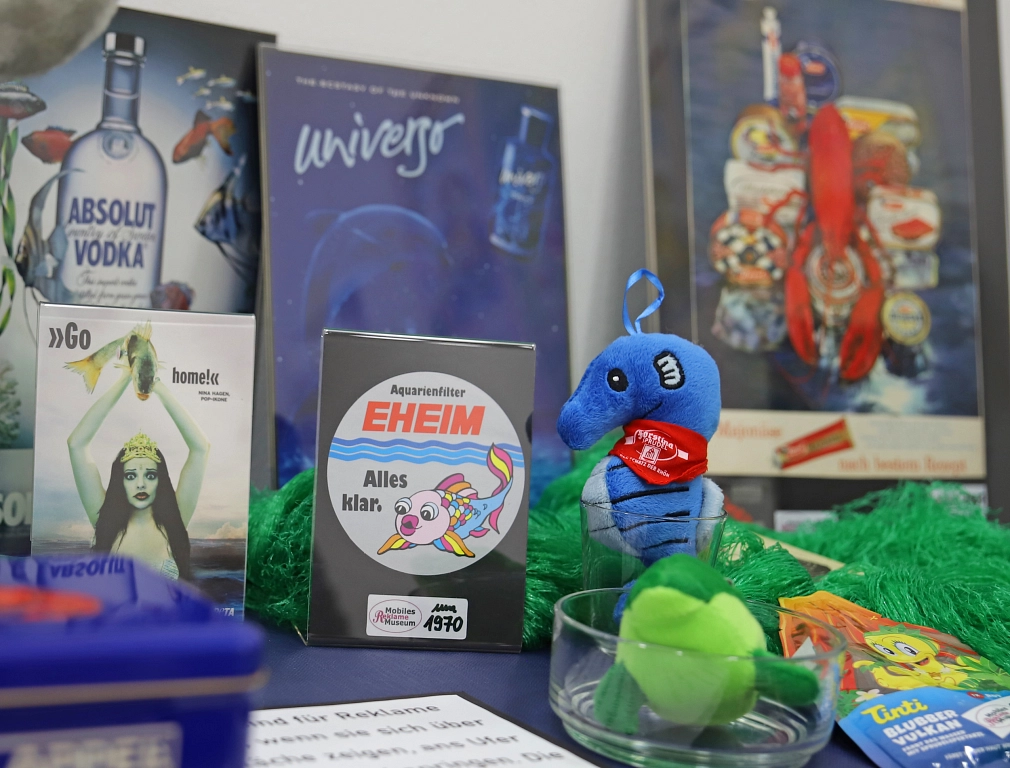 Zu sehen sind verschiedene Werbegegenstände der Ausstellung des Reklame-Museums. Zum Beispiel ein Seepferdchen oder Plakate mit Fischen.