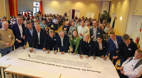 Eine Gruppe steht vor einem Tisch und unterzeichnet eine Erklärung des neuen Netzwerks für Demokratie und gegen Rechtsextremismus. © Patricia Grähling, Stadt Marburg
