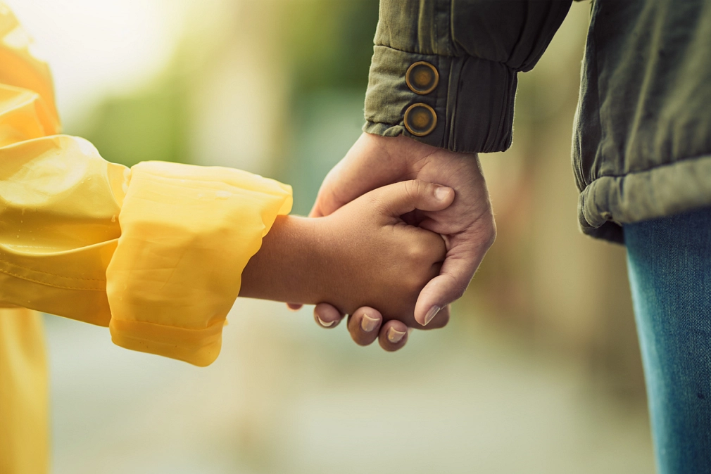 Die Hand eines Erwachsenen hält die eines Kindes. Die Hand einer erwachsenen Person hält eine Kinderhand. © iStock|PeopleImages