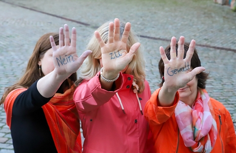 Nein zu Gewalt ist auf den Handinnenflächen der drei orange-gekleideten Frauen zu lesen. © Simone Batz, Stadt Marburg