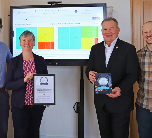 eGovSAD_Digital-Award 2024 Vier Personen stehen vor einem Bildschirm. Der Bildschirm zeigt eine Oberfläche mit mehreren Grafiken. Die zwei Personen in der Mitte halten eine Urkunde und einen Preis in der Hand. Es geht um den Digital-Award 2024.