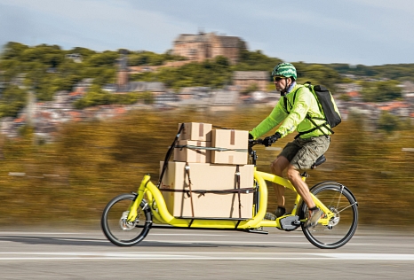 Ein Mann mit Elektro-Lastenrad transportiert viele Pakete, im Hintergrund ist das Marburger Schloss. © Universitätsstadt Marburg