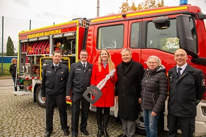 Feuerwehr Moischt nimmt neues Feuerwehrauto in Dienst. Das Bild zeigt Personen, die vor einem Feuerwehrauto stehen. In der Mitte steht eine Frau mit einem großen Schlüssel in den Händen.