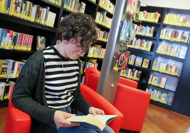 Eine junge Frau sitzt in einem roten Sessel in der Stadtbücherei, im Hintergrund sind mehrere Bücherregale zu sehen. Sie hält ein Buch in der Hand und liest.&nbsp;&copy;&nbsp;Patricia Grähling, Stadt Marburg