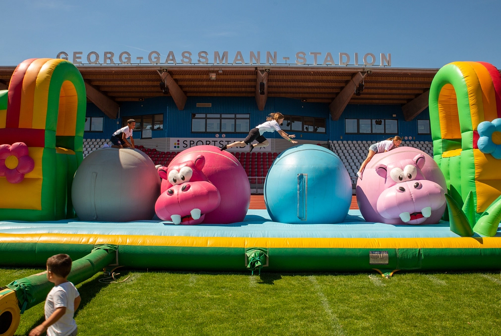 Kinder springen beim Fun Day im Georg-Gassmann-Stadion über riesige Hippos einer Hüpfburg.