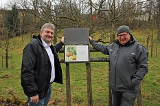Bürgermeister Wieland Stötzel (links) und Ludwig Schneider, Ortsvorsteher Ockershausen, zeigen ein Schild des Apfellehrpfads im Heiligen Grund. © Thomas Steinforth, Stadt Marburg