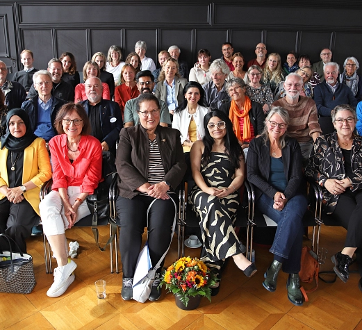 Gruppe_10 Jahre Portal Eine Gruppe von Menschen sitzt in einem Raum auf Stühlen.
