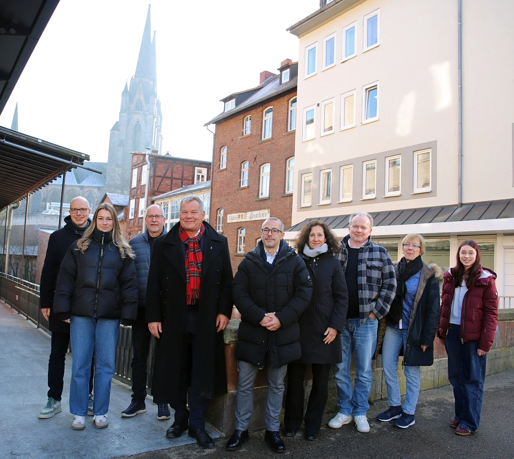 Eine Gruppe von Menschen steht in einer Straße. Im Hintergrund ist ein Kirchturm zu sehen.