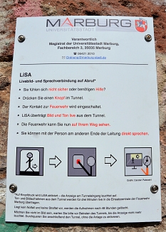 Am Tunneleingang hängt die Erklärung, wie „LiSA“ funktioniert. Wird sie von Pasant/innen per Knopfdruck eingeschaltet, weist eine Leuchttafel auf die Livebild-Übertragung hin. © Stadt Marburg, Birgit Heimrich