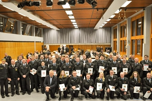 JHV 2026 FFW MR Eine große Gruppe von Feuerwehrfrauen und -männern stehen gemeinsam in einem Saal. Viele halten eine Urkunde in den Händen. Alle lächeln in die Kamera. Im Hintergrund sind weitere Personen zu sehen.