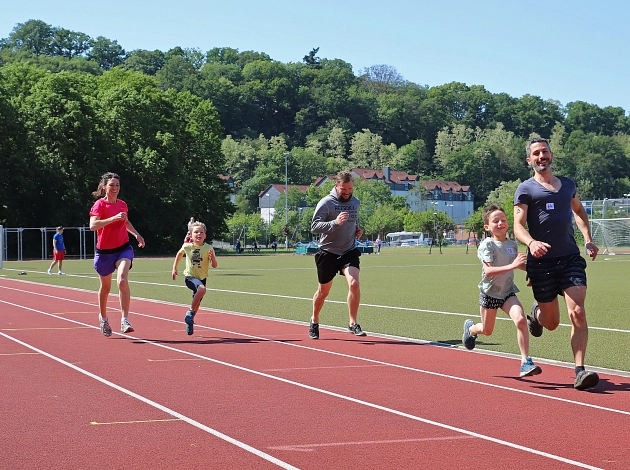 Eine Frau, zwei Männer und zwei Kinder laufen auf einer Laufbahn und lachen fröhlich.