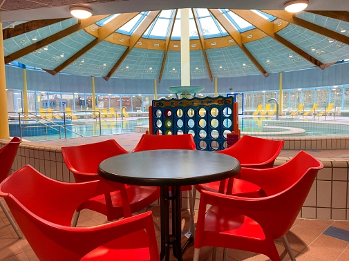 Kiosk AquaOase im AquaMar Sitzgruppe aus roten Stühlen und einem runden Tisch, im Hintergrund ist die Kuppel vom AquaMar mit dem Aktionsbecken darunter. © Simone Batz, Stadt Marburg