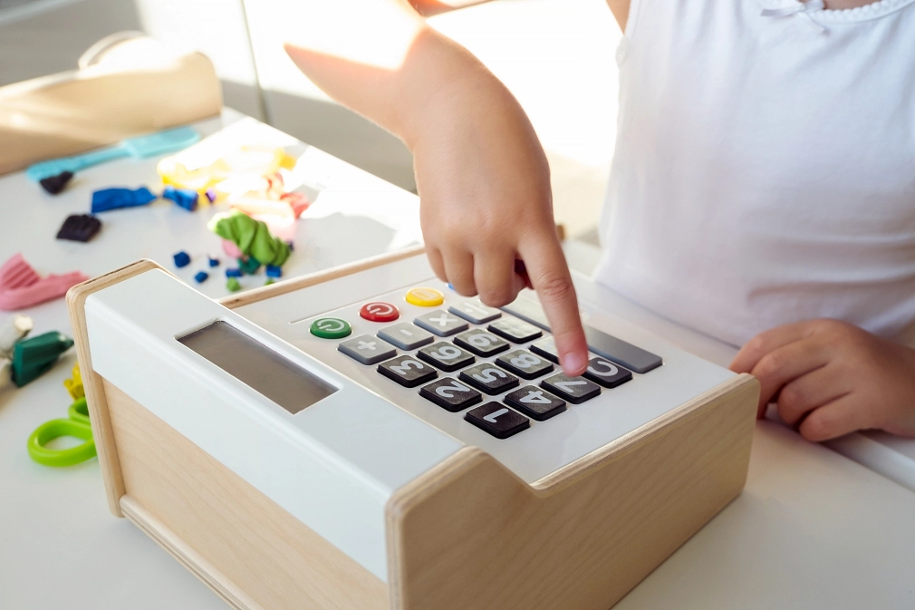 Kita-Gebühren Eine Kinderhand tippt auf die Tasten eine Spielzeug-Kasse. © istock/Valeriia Mitriakova