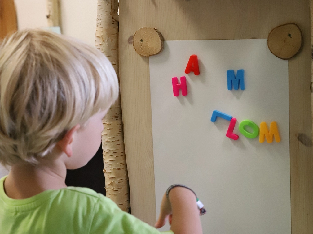 Ein Kind steht vor einer Holzwand, an der ein Papier hängt. Über das Papier verteilt finden sich Buchstaben.&nbsp;&copy;&nbsp;Stefanie Profus, i.A.d. Stadt Marburg