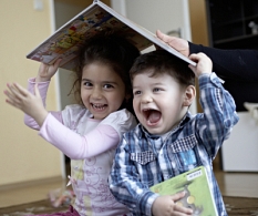 Zwei lachende Kleinkinder halten ein Bilderbuch über ihren Köpfen. © Stiftung_Lesen__Fotograf_Oliver_Ruether