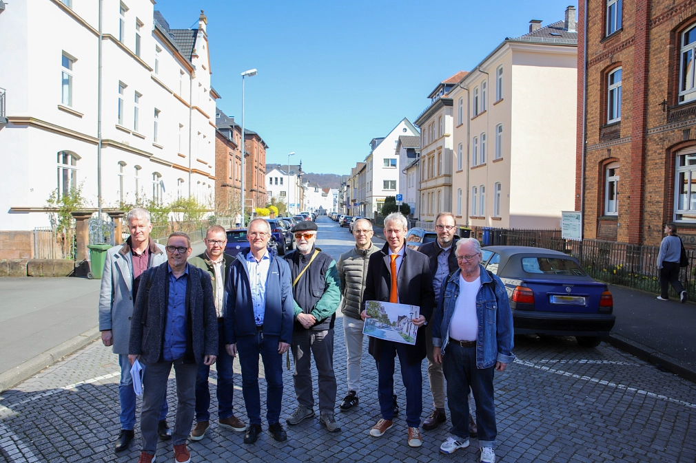 Neun Personen stehen in einer Straße und schauen in die Kamera. Eine Person hält ein Blatt in den Händen. Darauf ist eine Modellansicht der Straße zu sehen , auf der sie sich befinden.