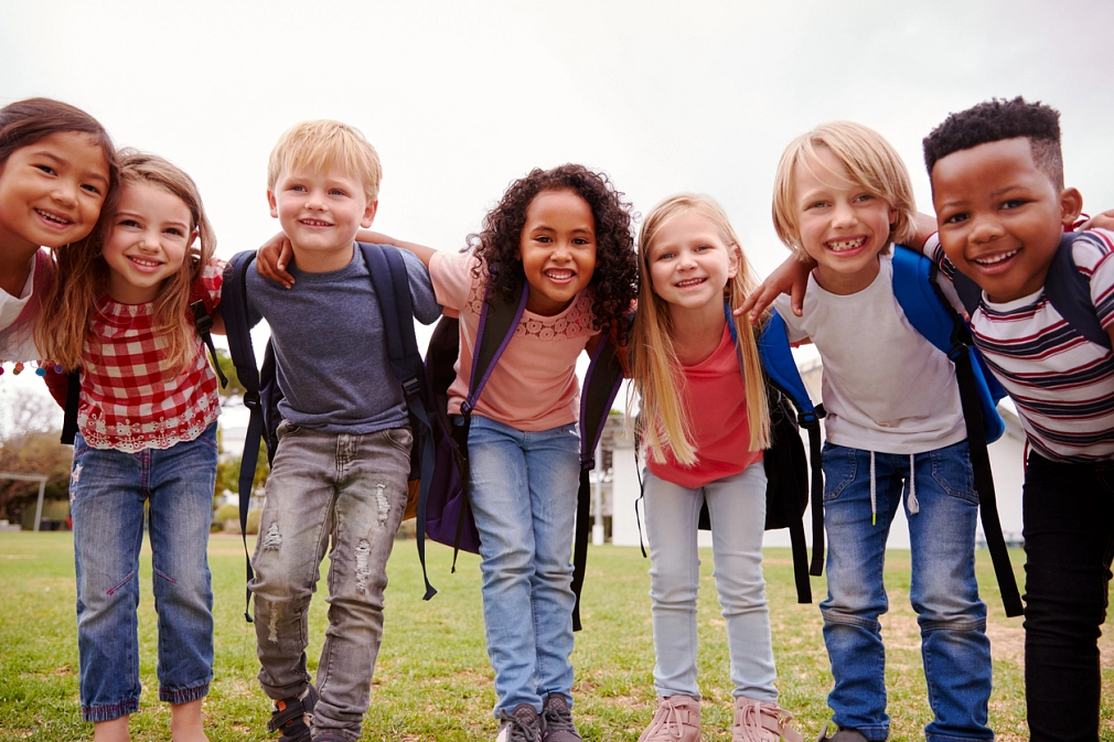 In der Pause: Eine Gruppe von lachenden Grundschüler*innen auf dem Rasen.