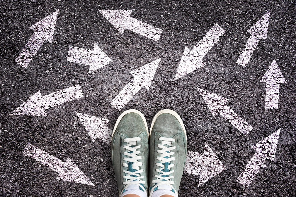 Marburg_Jugendberufshilfe_iStock_1136179001 Sneakerschuhe und Pfeile auf Asphaltgrund; die Pfeile zeigen in verschiedene Richtungen. © iStock/Delpixart