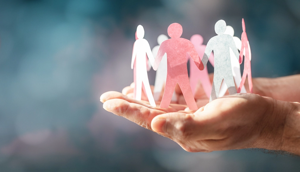 Marburg_Pädagogische Betreuung_Integration_Migration Gemeinschaft: Zwei Hände halten Figuren aus Papier, die sich die Hände reichen. © iStock/BrianAJackson