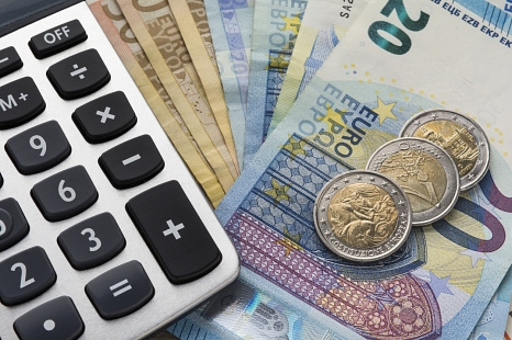 Thema Wohngeld und Wohngeld beantragen: Nahaufnahme eines Taschenrechner sowie Euro-Geldschein und Euro-Münzen von oben. © iStock / arsenisspyros