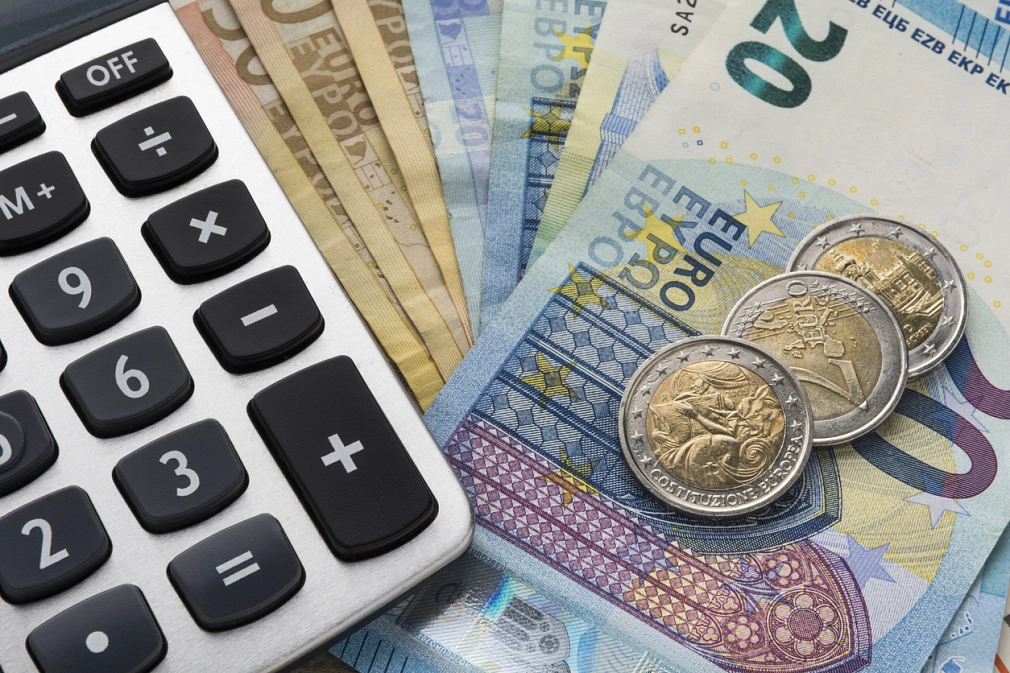 Thema Wohngeld und Wohngeld beantragen: Nahaufnahme eines Taschenrechner sowie Euro-Geldschein und Euro-Münzen von oben.&nbsp;&copy;&nbsp;iStock / arsenisspyros