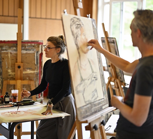 Marburger Sommerakademie Zwei Personen stehen vor Staffeleien und an Tischen und malen Bilder.