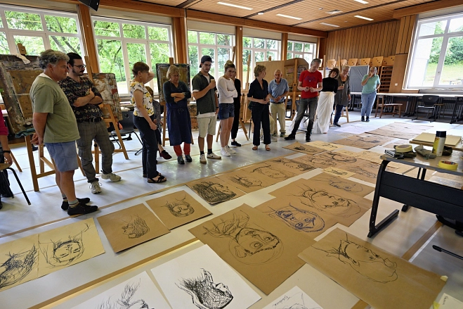 Marburger Sommerakademie: Eine Gruppe von Menschen begutachtet die Zeichnungen, die vor ihnen auf dem Boden liegen.