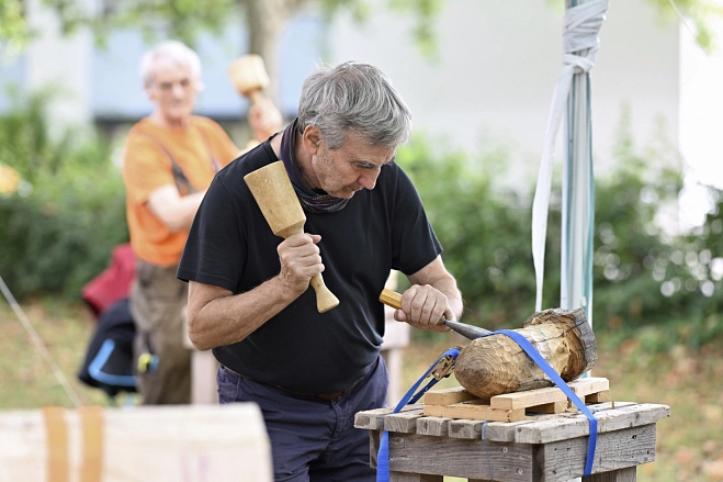 Marburger Sommerakademie: Mensch bearbeitet einen Holzblock mit einem Meißel.