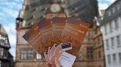Flyer des MarburgPasses werden hochgehalten. Dahinter ist das Marburger Rathaus zu sehen.