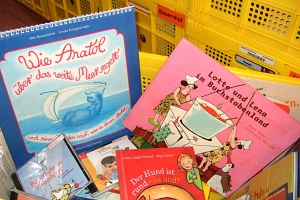 Eine gelbe Kiste, gefüllt mit Bilderbüchern für Kinder im Kita- und Grundschul-Alter. Im Hintergrund sind weitere gelbe Kisten gestapelt - eine trägt die Aufschrift "Bauernhof".