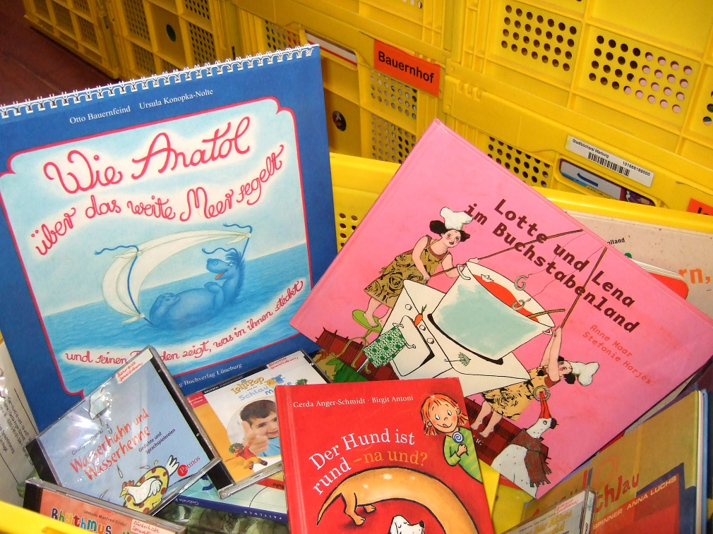 Medienkisten für Kitas und Schulen Eine gelbe Kiste, gefüllt mit Bilderbüchern für Kinder im Kita- und Grundschul-Alter. Im Hintergrund sind weitere gelbe Kisten gestapelt - eine trägt die Aufschrift "Bauernhof". © Universitätsstadt Marburg